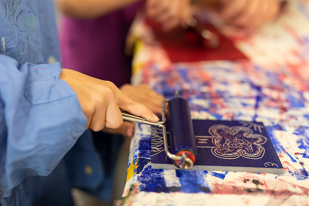Kind beim Arbeiten mit blauer Farbe, Rolle und Druckplatte