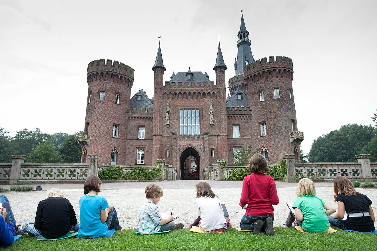 Kinder sitzen im Kutschenrondell und zeichnen das Schloss