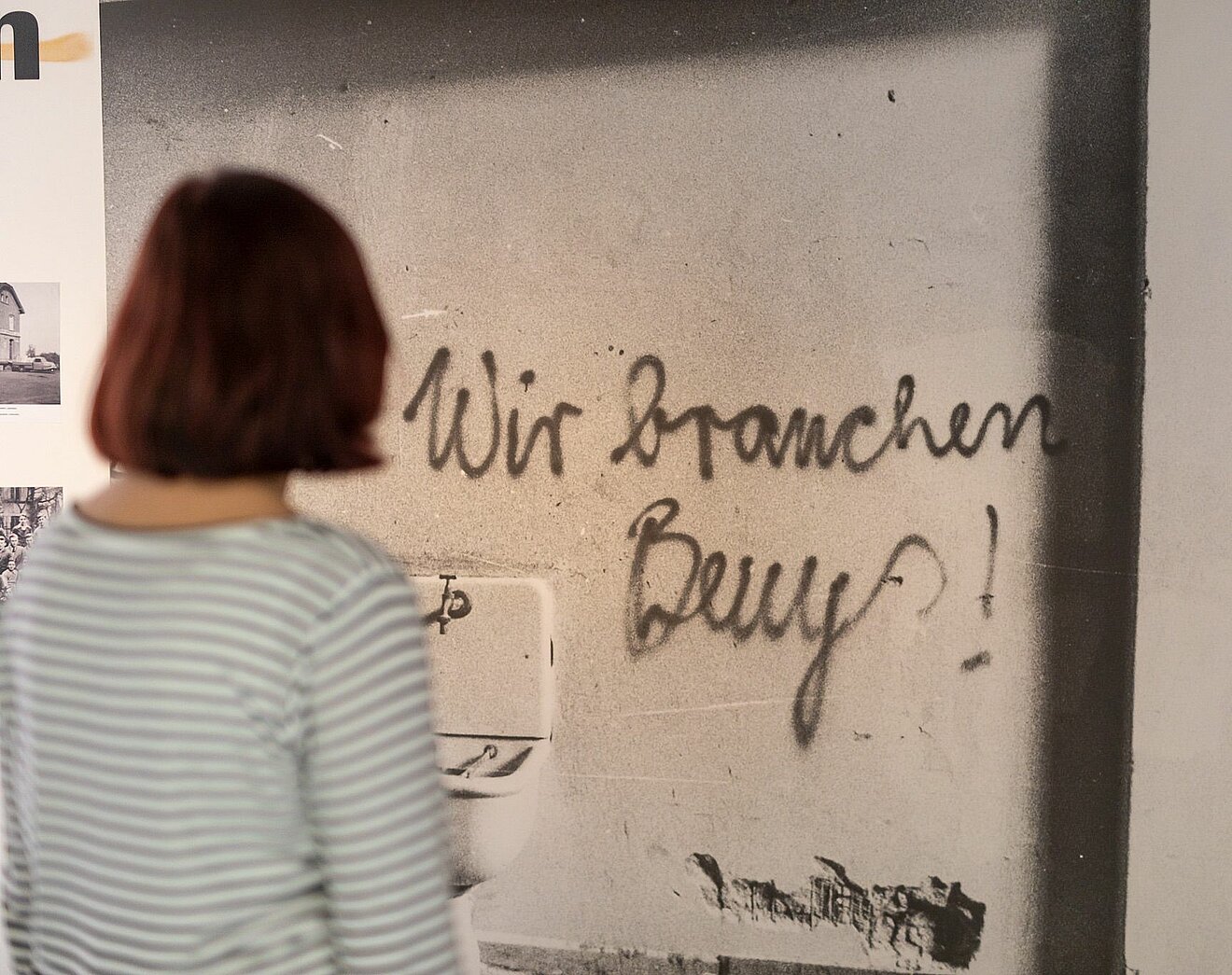 Besucherin vor dem Foto eines Graffitis mit dem Satz "Wir brauchen Beuys"